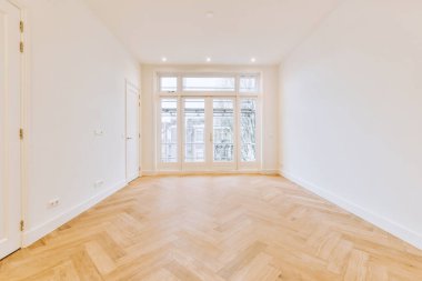 Büyük balkon pencereleri ve ahşap parke zemini olan boş beyaz odanın içi.