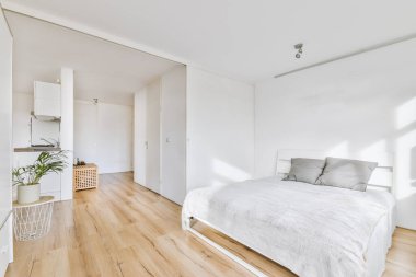 Minimalist yatak odası iç tasarımı yumuşak yataklı, duvarda gri yastıklar ve doğal güneş ışığı olan beyaz gömme dolap.