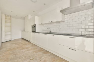 Beyaz duvarları ve fayanslı zemini olan geniş, parlak bir mutfak.