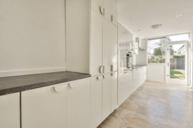 Beyaz duvarları ve fayanslı zemini olan geniş, parlak bir mutfak.