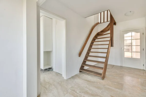 A bright, empty room with white walls and a staircase, as well as a stylish tiled floor