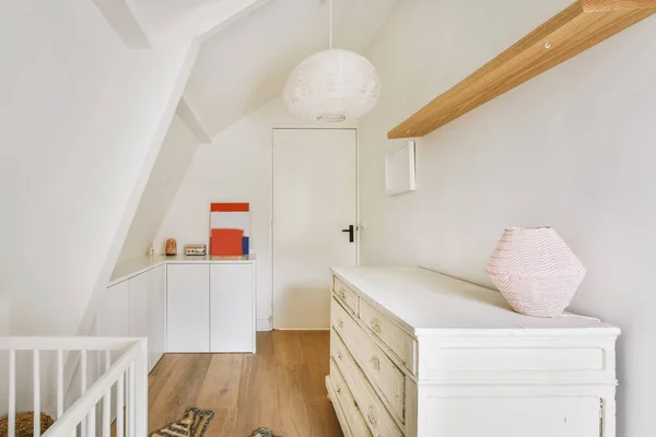 Childrens attic room with white walls and storage space, parquet flooring and a white door with a black handle