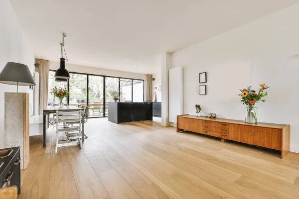 Table with chairs and flowers located near lounge area and kitchen in spacious room of contemporary apartment