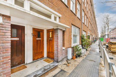 Tabelaları, arabaları, kaldırımları ve ahşap kapıları olan tuğla binanın önü daireye çıkıyor.