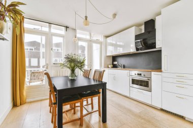 Stüdyo dairesinin modern minimalist tarzı iç tasarımı açık beyaz mutfak ve yemek masası ve sandalyeleri tavan arası lambasıyla aydınlatılmış.