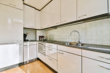 Modern bir apartman dairesinde beyaz dolapları ve ahşap zemini olan bir ev mutfağının modern iç tasarımı.