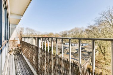 Dar tuğlalı balkon, beyaz metal parmaklıklar, tahta sandalye ve avlu manzarası.