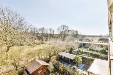Doğanın panoramik manzarası, bir apartmanın balkonundan ağaçlarla ve ahşap binalarla dolu avlu.