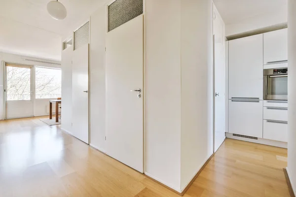 Hall with white walls and doors leading to a kitchen with parquet floors in a modern apartment