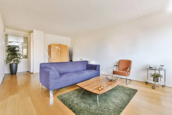 Square table on rug next to purple sofa and wooden cabinet in stylish living room of modern apartment