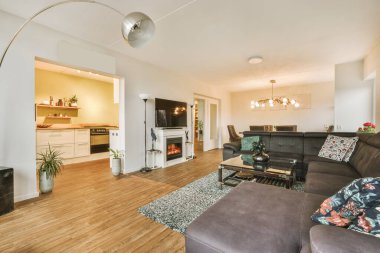 Mutfağın yakınındaki açık oturma odasındaki şöminenin yanındaki zarif avizenin altında yumuşak yastıklı büyük bir kanepe.