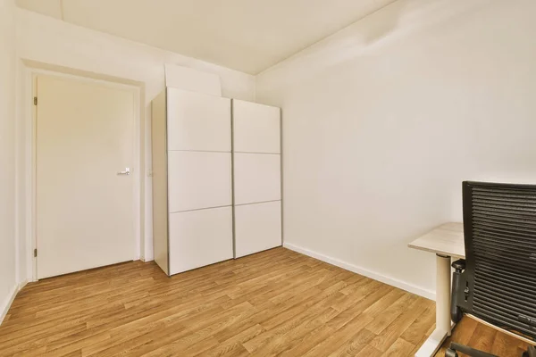 白い壁とテーブルと黒いアームチェア付きの木製の床の部屋の白いワードローブ — ストック写真