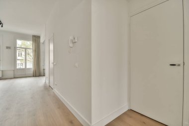 Giriş kapısı, beyaz duvarları ve parke zemini lambayla aydınlatılmış, geometrik tasarımı olan boş, modern bir daire.