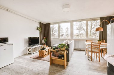 Çağdaş dairenin geniş odasındaki dinlenme odası ve mutfağın yakınındaki sandalyeli ve çiçekli masa.