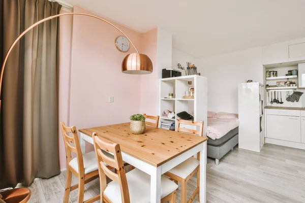 Table with chairs and flowers located near lounge area and kitchen in spacious room of contemporary apartment