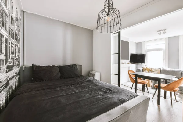 Minimalist interior design of small bedroom with soft bed placed in corner and wooden table with lamp illumination