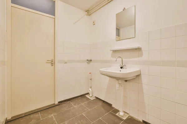 Wall hung toilet and small sink in corner in lavatory room with beige tile