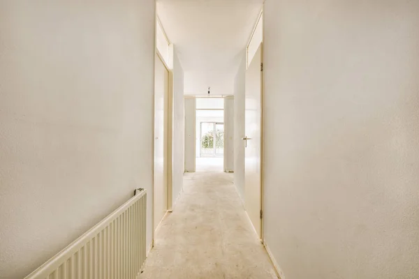 木の床の上に白い壁と輝くランプの多くのドアを持つ光の狭い廊下 — ストック写真
