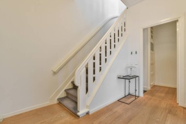 Minimalist iç tasarımı olan modern lüks dairenin ikinci katına çıkan ahşap merdivenli beyaz koridor.