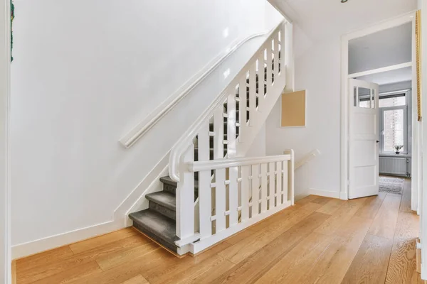 White hallway with wooden stairway leading to second floor of modern luxury apartment with minimalist interior design