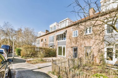 Arabaları, ağaçları ve fenerleri olan boş bir kaldırımdan panorama manzaralı evler.