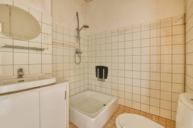 Eski püskü bej duvarları, bölmeleri ve beyaz kapısı olan çağdaş banyonun içi.