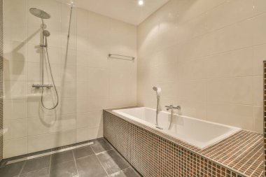 Küvet, banyo kutusunun yanında, modern banyoda cam kapılı, beyaz fayanslı duvarlı.