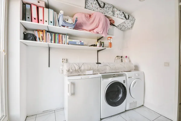 White room with washer and dryer, tiled floor and shelves with folders, baskets and bags
