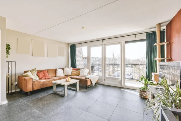 Interior of light living room with stylish furniture and decorations and glass door and windows leading to balcony on sunny day