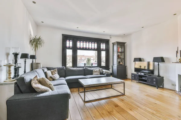 Simple living room interior with large black framed windows and gray sofa in front of TV