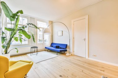 Modern apartmandaki geniş minimalist tarzda oturma odasında halı ve masaya yakın rahat bir kanepe.