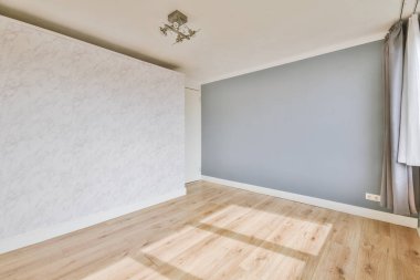 Gri duvarı, ahşap zemini ve avizesi olan geniş boş bir oda.