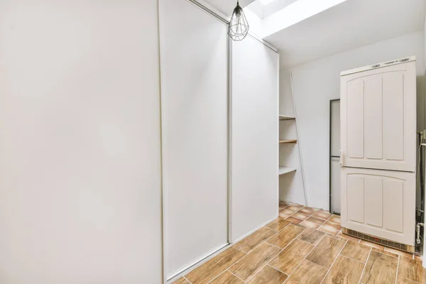 Empty narrow room with storage space, white cabinets, chandelier and wooden floor