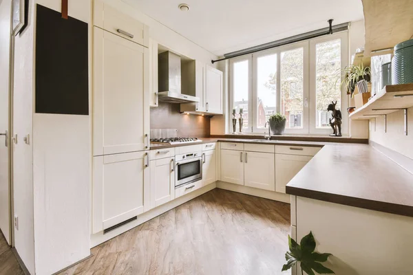 İyi organize edilmiş küçük bir ev mutfağı pencerenin altında lavabo, sobalı hafif mobilyalar ve kentsel apartmanda buzdolabı var.