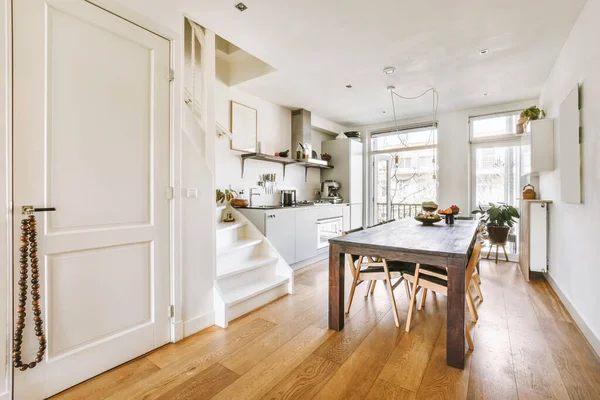 白い階段のあるモダンな明るいアパートのキッチン家具の横にある木製のテーブルと快適な椅子 — ストック写真
