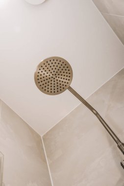 Duş musluğu modern dairede hafif tuvaletin beyaz fayanslı duvarında asılı.