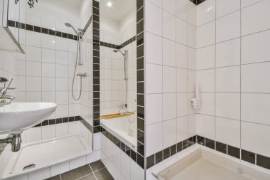 Modern banyoda aynalı lavabo ve cam kapılı duş kutusu ve beyaz fayanslı duvarlar.