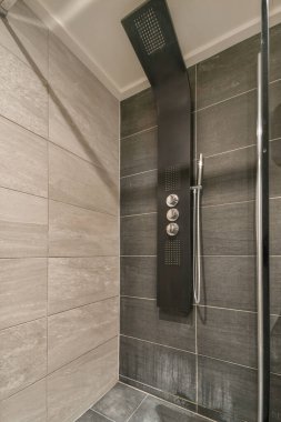 Banyonun minimalist iç kısımlarına asılmış siyah duvar ve üst rafta çiçekler var.