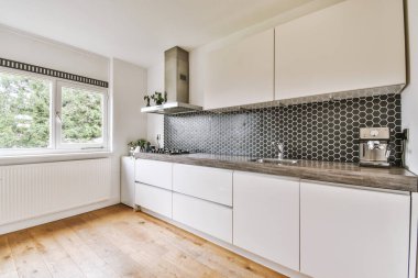 Geniş pencereli hafif küçük ev mutfağı modern kentsel dairede dolaplar ve raflarla donatılmış.