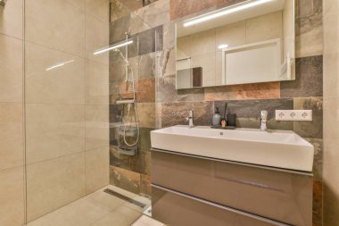 Çağdaş dairenin küçük fayanslı banyosunda lavabo ve duş arasında bulunan sifon tuvaleti