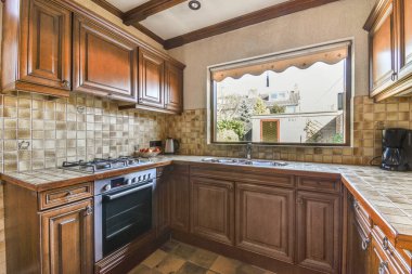 Fragment of interior of brown narrow home kitchen with minimalist style white furniture with sink and stove