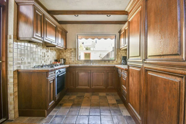 Fragment of interior of brown narrow home kitchen with minimalist style white furniture with sink and stove