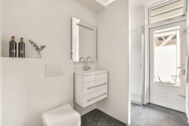 Modern sifon tuvaleti ve seramik lavabo aynanın yanındaki beyaz fayanslı duvarlara ve evdeki küçük tuvaletteki havluya monte edildi.