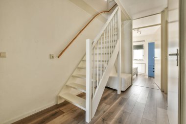 Minimalist iç tasarımı olan modern lüks dairenin ikinci katına çıkan ahşap merdivenli beyaz koridor.