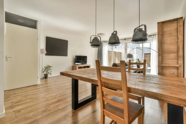 Günümüz minimalist tasarımı. Hafif stüdyo dairesinin ahşap masası ve oturma odası ile beyaz duvarları ve parke zemini arasında yemek masası ve sandalyeleri var.