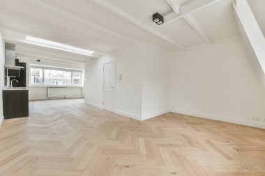 Pencereleri ve ahşap parke zemini olan boş beyaz mutfağın içi.