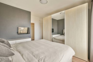 Minimalist komodini, televizyonu ve geniş panoramik penceresi olan ferah, parlak bir yatak odası.