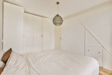 Rahat bir yatağın yanında kitap ve lamba bulunan eski komodinin yanında modern yatak odasının penceresine karşı dekorasyonlu bir raf.