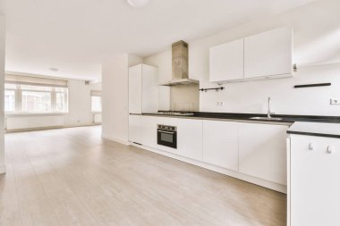 Pencereleri ve ahşap parke zemini olan boş beyaz mutfağın içi.