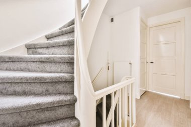 Minimalist iç tasarımı olan modern lüks dairenin ikinci katına çıkan ahşap merdivenli beyaz koridor.